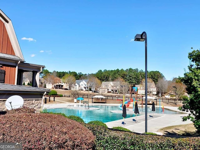 community pool with a patio, playground community, a water play area, fence, and a residential view