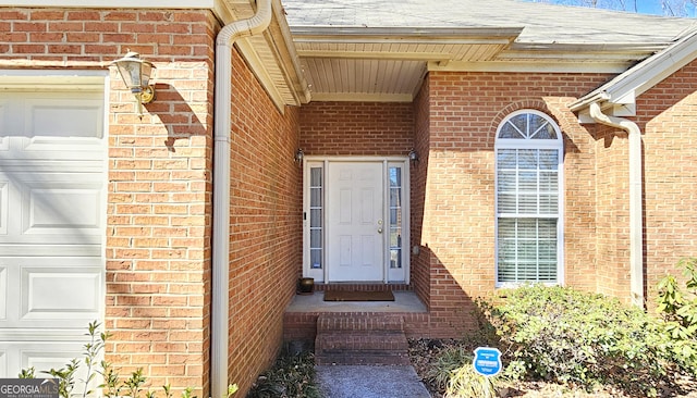 property entrance with brick siding, an attached garage, and roof with shingles