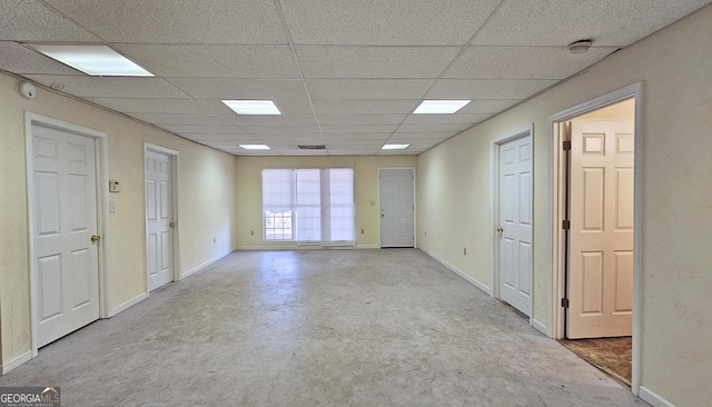 unfurnished room with concrete flooring, a drop ceiling, and baseboards