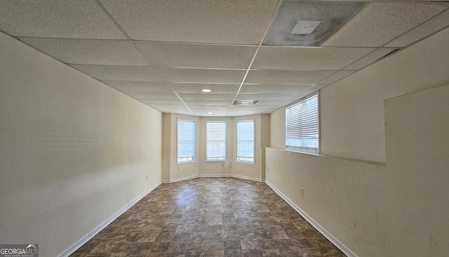 unfurnished room featuring stone finish floor, a drop ceiling, and baseboards