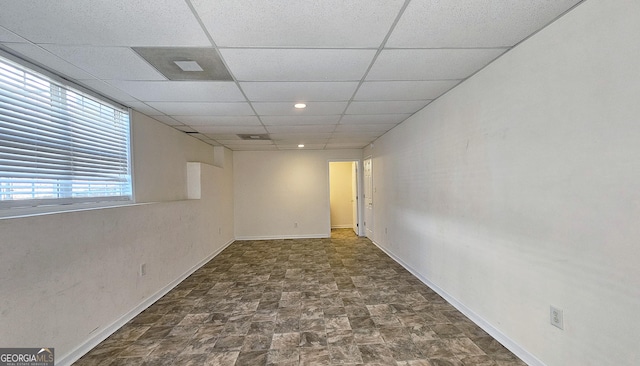 empty room with a paneled ceiling, stone finish flooring, and baseboards