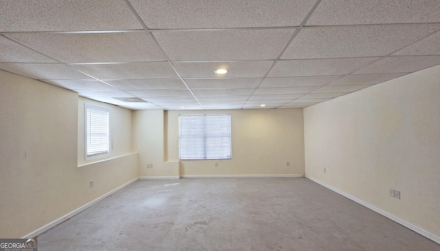 spare room featuring baseboards, a drop ceiling, and concrete flooring