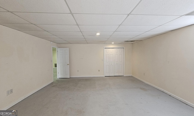 unfurnished room featuring concrete flooring, a drop ceiling, and baseboards