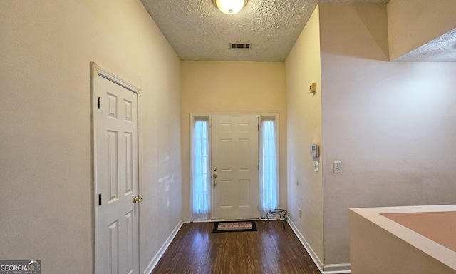 foyer entrance with dark wood-type flooring, visible vents, a textured ceiling, and baseboards