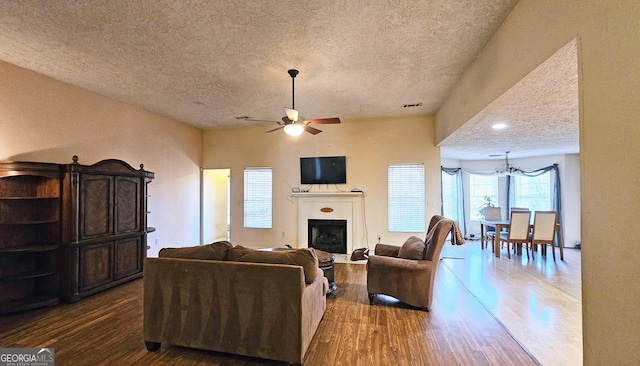 living area with a ceiling fan, a fireplace, a textured ceiling, and wood finished floors