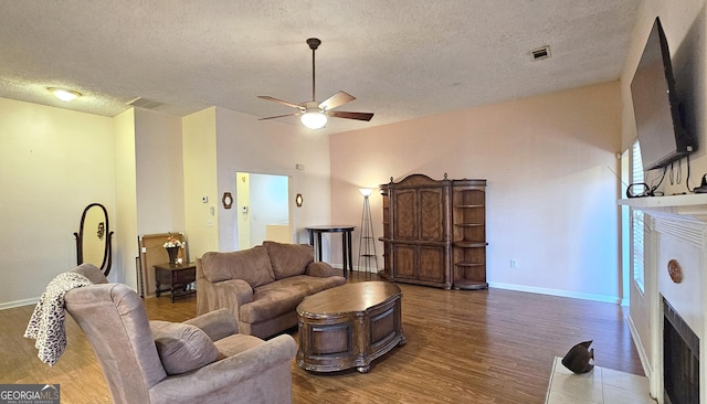 living room featuring a fireplace, ceiling fan, a textured ceiling, wood finished floors, and baseboards