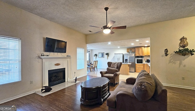 living area with light wood finished floors, baseboards, a ceiling fan, a tile fireplace, and a textured ceiling