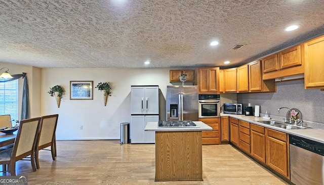 kitchen featuring light wood-style flooring, a center island, stainless steel appliances, light countertops, and a sink