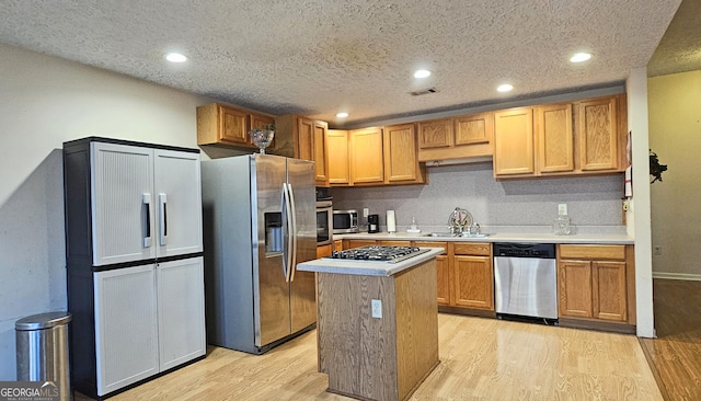 kitchen with stainless steel appliances, light countertops, a sink, and a kitchen island