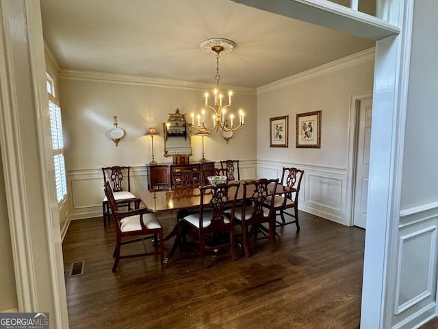 dining room featuring crown molding, visible vents, a decorative wall, dark wood-type flooring, and a chandelier