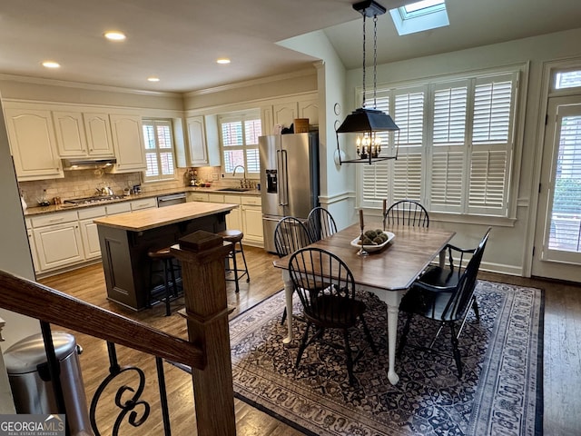 dining room with a skylight, ornamental molding, wood finished floors, a notable chandelier, and recessed lighting