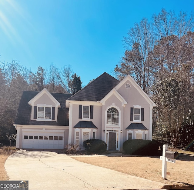 traditional home featuring driveway, a shingled roof, an attached garage, and stucco siding