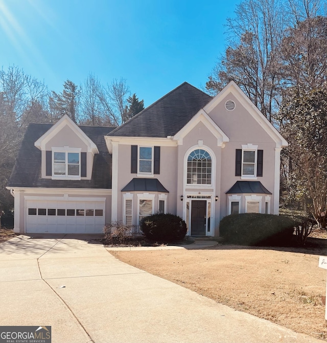 traditional home with a garage, roof with shingles, driveway, and stucco siding