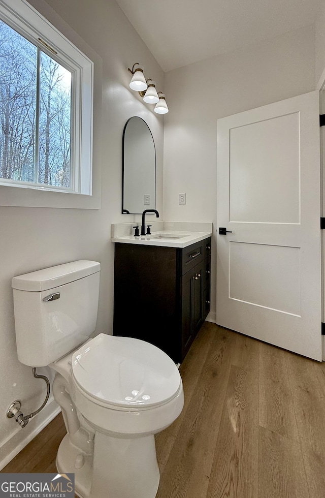 half bathroom featuring toilet, wood finished floors, and vanity