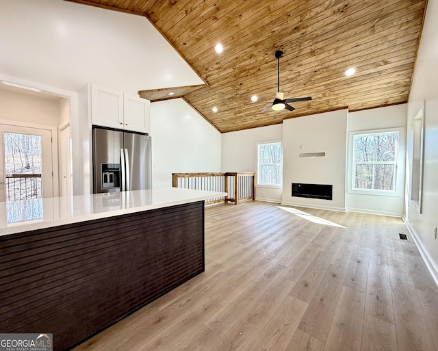 kitchen featuring light wood finished floors, stainless steel fridge, white cabinets, open floor plan, and light countertops