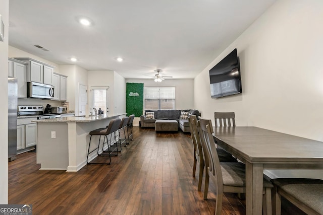 kitchen featuring stainless steel appliances, gray cabinets, a center island with sink, and light stone countertops