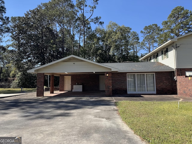 view of front of property featuring an attached carport, brick siding, driveway, roof with shingles, and a front lawn