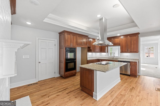 kitchen with light stone counters, a kitchen island, black appliances, a tray ceiling, and island exhaust hood