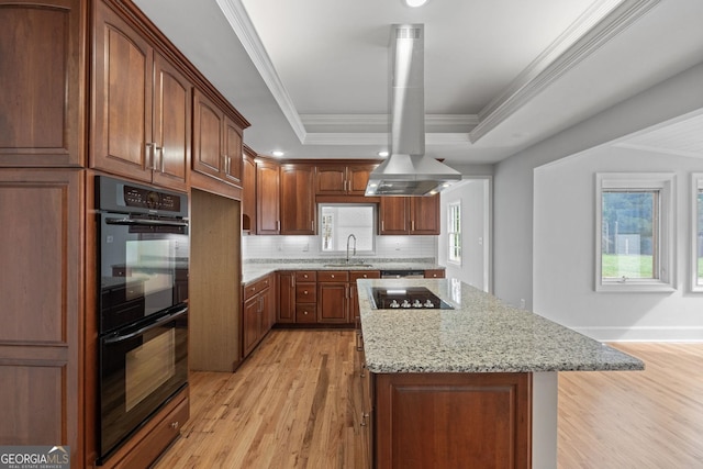 kitchen featuring a raised ceiling, light stone countertops, island exhaust hood, black appliances, and a sink