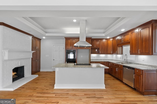 kitchen with a sink, a center island, black appliances, light wood finished floors, and a raised ceiling