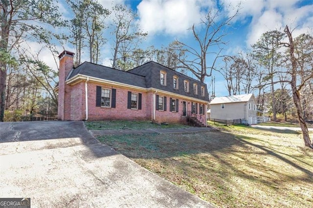 exterior space with driveway, a shingled roof, a chimney, a front yard, and brick siding