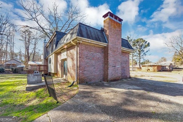 view of property exterior with brick siding, a chimney, mansard roof, a shingled roof, and a deck