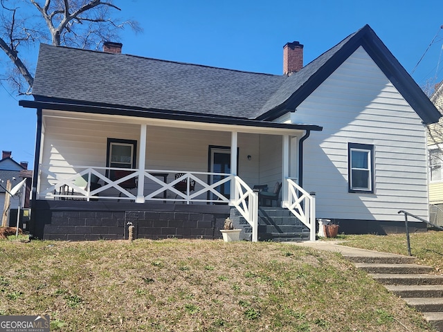 back of house with a shingled roof, covered porch, a yard, and a chimney