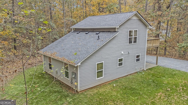 exterior space featuring roof with shingles, a lawn, and a view of trees