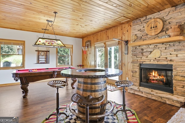 game room with wooden ceiling, dark wood finished floors, wood walls, and a stone fireplace