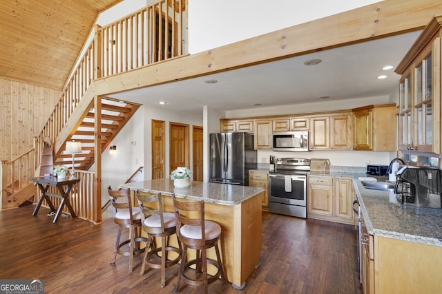 kitchen featuring stone counters, a sink, appliances with stainless steel finishes, a center island, and dark wood finished floors