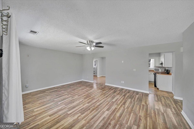 unfurnished living room featuring visible vents, ceiling fan, a textured ceiling, light wood-type flooring, and baseboards