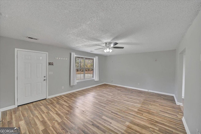 interior space featuring ceiling fan, a textured ceiling, visible vents, baseboards, and light wood finished floors