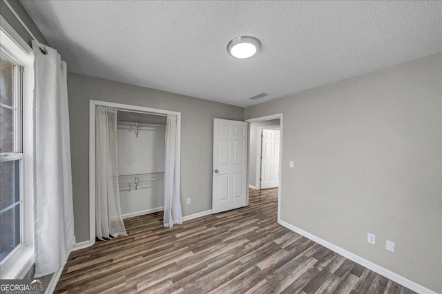 unfurnished bedroom with baseboards, visible vents, dark wood-type flooring, a textured ceiling, and a closet