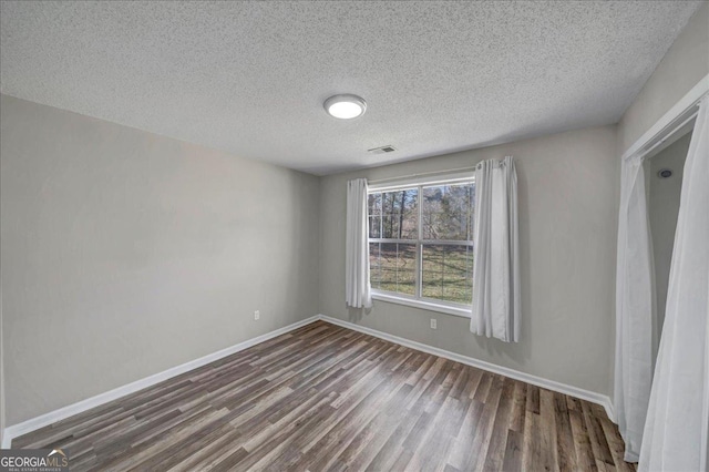 unfurnished bedroom with dark wood-style floors, a textured ceiling, visible vents, and baseboards