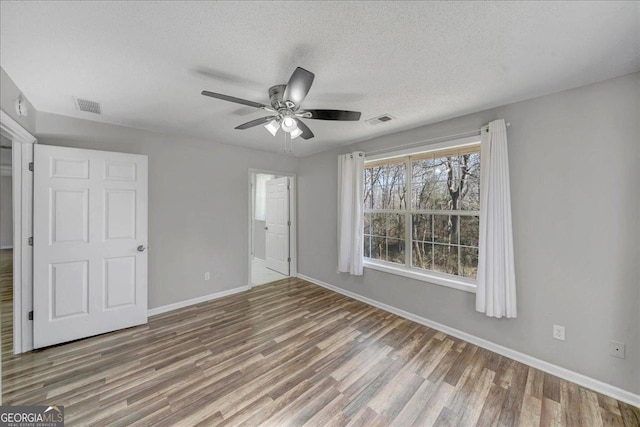 unfurnished bedroom with a textured ceiling, wood finished floors, visible vents, and baseboards