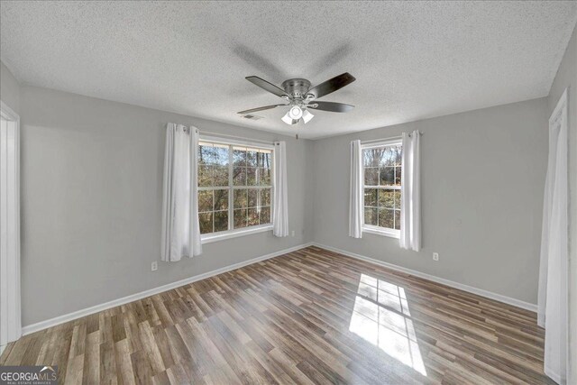 spare room with a healthy amount of sunlight, visible vents, and wood finished floors