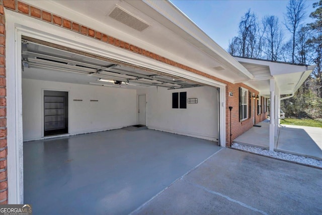 exterior space with a garage, driveway, brick siding, and a patio area