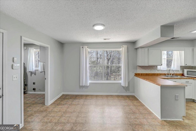 kitchen with white microwave, a peninsula, a sink, white cabinets, and wooden counters