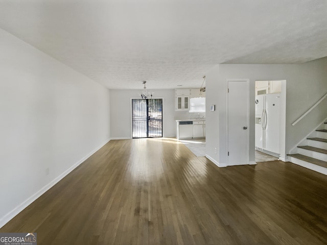 unfurnished living room with dark wood finished floors, stairway, baseboards, and an inviting chandelier