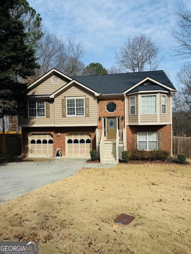 split foyer home featuring aphalt driveway, brick siding, fence, and an attached garage