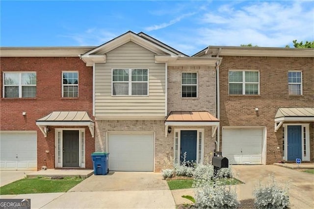 townhome / multi-family property with metal roof, an attached garage, brick siding, driveway, and a standing seam roof