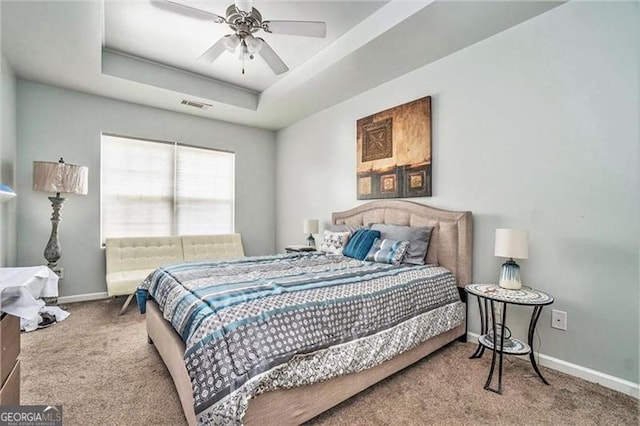 carpeted bedroom with a tray ceiling, visible vents, ceiling fan, and baseboards