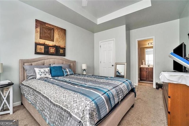 bedroom featuring ceiling fan, connected bathroom, light colored carpet, baseboards, and a tray ceiling