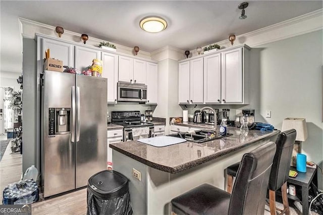 kitchen with a breakfast bar area, stainless steel appliances, a peninsula, white cabinets, and light wood-type flooring