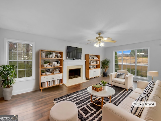 living area featuring a ceiling fan, a fireplace, baseboards, and wood finished floors