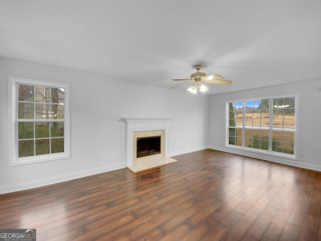 unfurnished living room featuring ceiling fan, dark wood-type flooring, a fireplace, and baseboards