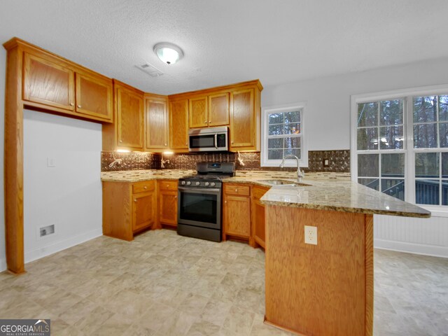 641 Morningside Dr, Stockbridge, GA 30281 - kitchen with brown cabinetry, appliances with stainless steel finishes, light stone counters, a peninsula, and a sink