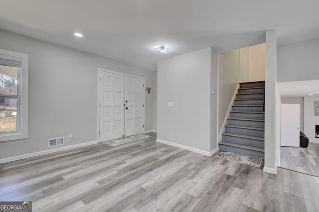 entryway featuring a fireplace, visible vents, light wood-style floors, baseboards, and stairs