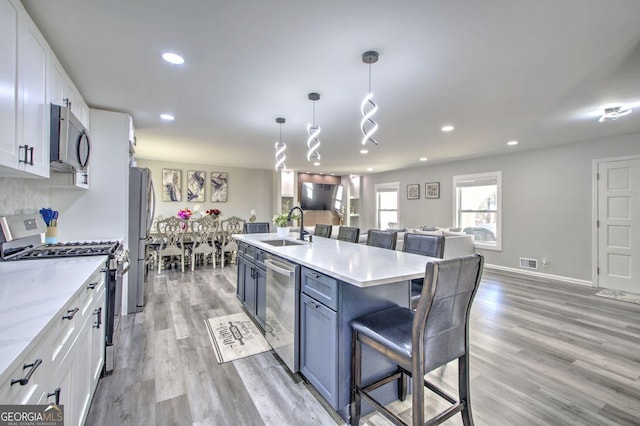 kitchen featuring stainless steel appliances, a sink, white cabinets, open floor plan, and a kitchen bar