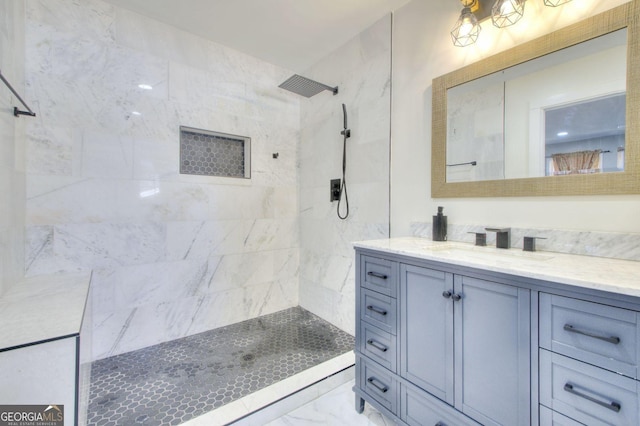 bathroom featuring marble finish floor, tiled shower, and vanity